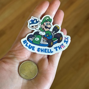May include: A blue and green sticker with a cartoon image of Mario and a blue shell. The sticker says "Blue Shell The 7% "