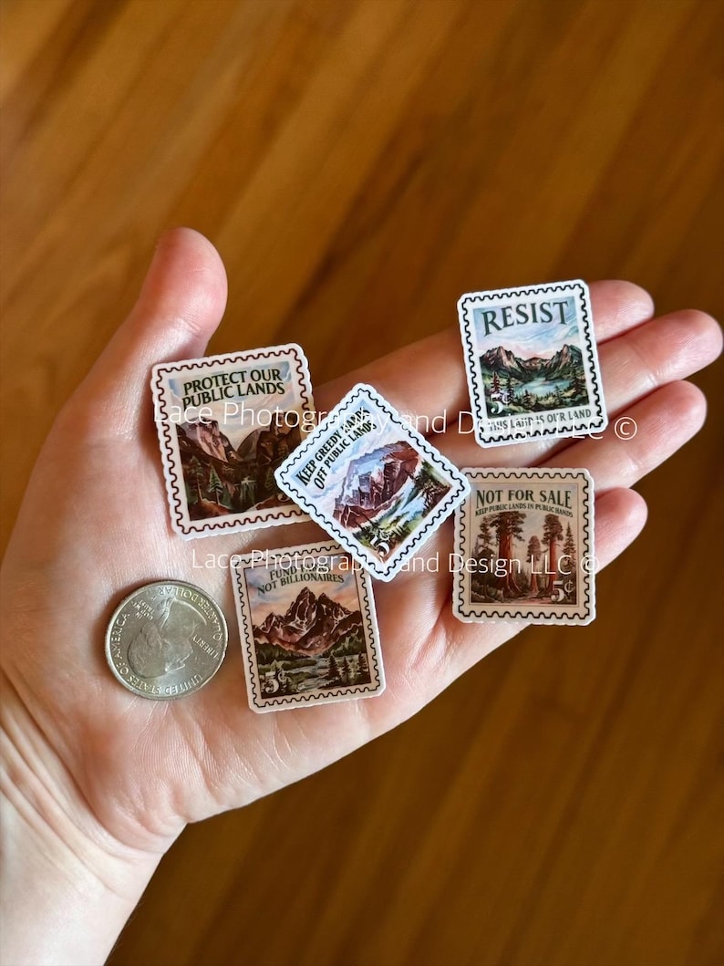 May include: A collection of miniature postage stamps with mountain and forest landscape designs. The stamps feature text such as "Protect Our Public Lands" and "Resist". A quarter is also visible.