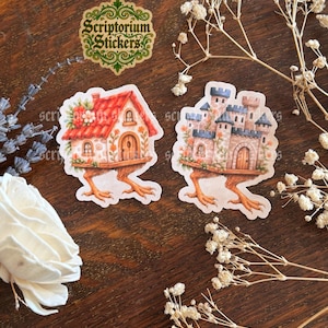 May include: Two whimsical stickers: a house with a red roof and a castle, both perched on bird-like feet. The house features floral accents and a wooden door. The castle has blue and tan turrets. A sticker with the text "Scriptorium Stickers" is also visible.