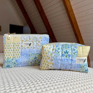 May include: Two quilted pouches with floral and patchwork designs. The larger pouch has a yellow and white gingham pattern, blue floral print, and a lace trim. The smaller pouch has a similar design. Both have gold zips and a "Gooseberry Atelier" label.