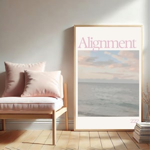 May include: A framed art print with the word "Alignment" in pink and blue lettering. The print features a serene ocean scene with a pastel sky. A light pink bench with two pillows sits to the left of the print. The number "222" is at the bottom of the print.