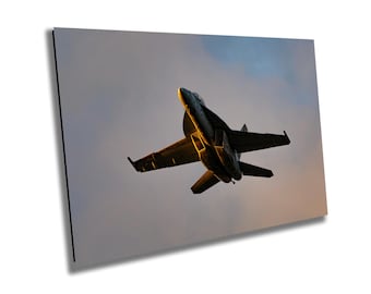 May include: A black fighter jet flies against a cloudy sky at sunset. The jet is silhouetted against the orange and yellow sky.