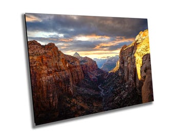 May include: A landscape print featuring a canyon scene with towering red rock formations. The sky is filled with dramatic clouds, and the sunlight illuminates the canyon walls. The print captures the natural beauty of the landscape.