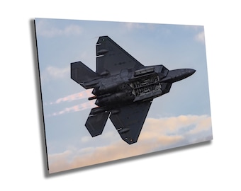 May include: A black fighter jet with afterburners on, flying in a cloudy sky.