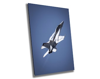 May include: A grayscale image of a jet fighter soaring through a clear, blue sky. The aircraft is angled upward, leaving a vapor trail. The jet's wings and tail are visible, showcasing its aerodynamic design.