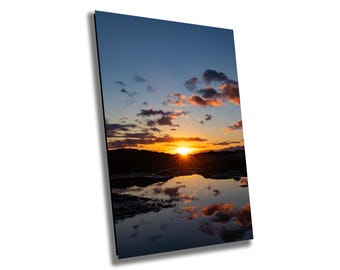May include: A vibrant sunset over a body of water, with the sun reflecting off the surface. The sky is a mix of orange, pink, and blue, with fluffy clouds.