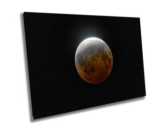 May include: A rectangular wall art print featuring a lunar eclipse against a solid black background. The moon displays a gradient of colors, transitioning from a bright white crescent at the top to a deep, dark reddish-orange hue across the surface.