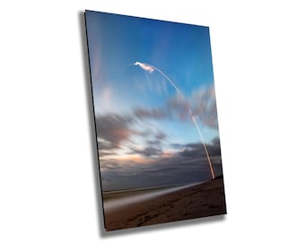 May include: A photograph of a rocket launching into a blue sky with streaking clouds. The rocket leaves a bright trail of light as it ascends from the beach, creating a dynamic and awe-inspiring scene.