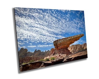 May include: A large, flat, red rock formation resembling a spaceship, with a dramatic, blue sky filled with white clouds in the background.