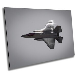 May include: A gray fighter jet flies through the air, leaving a white vapor trail behind it. The jet is in mid-air, with its wings spread out and its nose pointed towards the horizon.