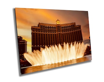 May include: A large, beige hotel with many windows and a tall tower at the front. The hotel is lit up at night and there are many fountains in front of it. The fountains are shooting water high into the air, creating a beautiful display of light and water.