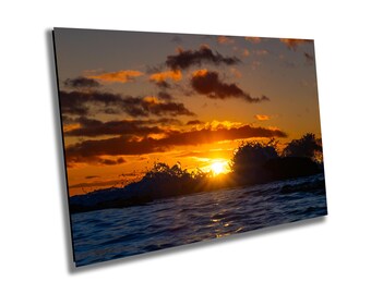 May include: A vibrant sunset over the ocean with waves crashing in the foreground. The sky is a mix of orange, yellow, and pink, with dark clouds adding depth. The sun is setting behind the waves, creating a warm glow.