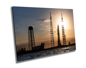 May include: Silhouette of a rocket on a launchpad at sunset. The rocket is tall and slender, with a pointed nose cone. The launchpad is a tall metal structure with a series of platforms. The sun is setting in the background, casting a warm glow over the scene.