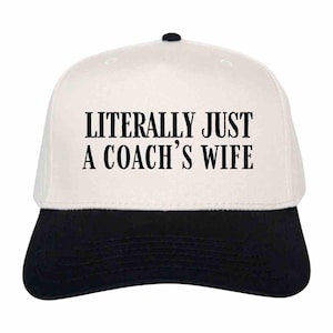 May include: White baseball cap with a black brim. The front of the cap has black text that reads "LITERALLY JUST A COACH'S WIFE."