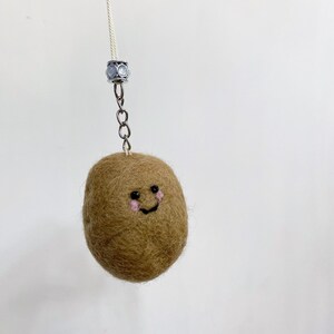 Può includere: Un ciondolo a forma di kiwi fatto a mano in feltro marrone con un volto sorridente, guance rosa e occhi neri. Il kiwi è attaccato a una catena d'argento e a un filo bianco, perfetto per un portachiavi o un accessorio per borse.