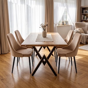 Peut inclure: Une table à manger rectangulaire en bois avec une finition brun clair et une base en métal noir en forme de V. Quatre chaises rembourrées en velours beige avec un capitonnage vertical et des pieds en métal noir entourent la table.