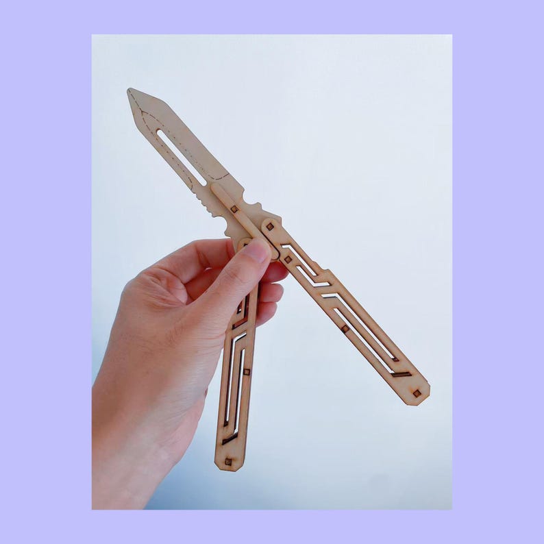 May include: A wooden butterfly knife with a light brown finish. The knife is held open, revealing a blade and two handles with geometric cutouts. The design features a series of straight lines and rectangular shapes.