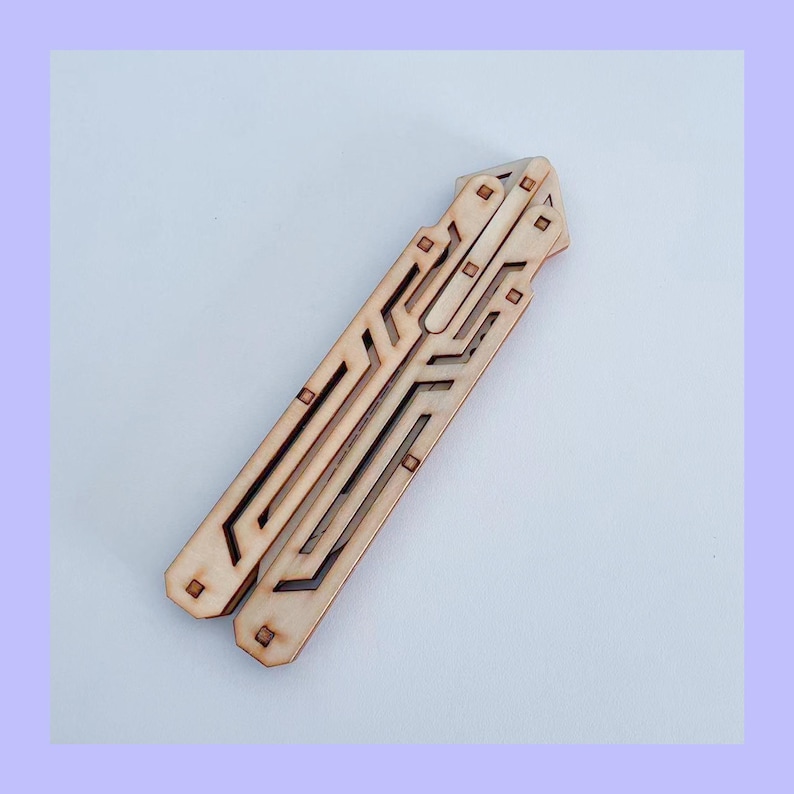 May include: A wooden butterfly knife trainer with a laser-cut design. The trainer is made of light brown wood and features a series of geometric cutouts and square accents. The design is symmetrical and the trainer is shown open.