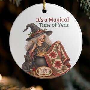 May include: A round white ceramic ornament featuring a witch with curly hair and a hat stirring a cauldron. A black cat sits nearby. The text reads It's a Magical Time of Year and Christmas 2026. The witch holds a quilt with a poinsettia pattern.