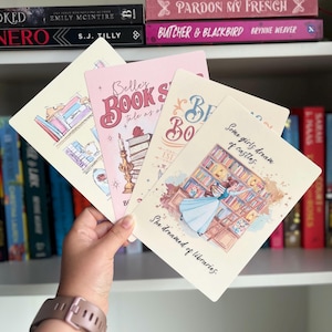 May include: A collection of four rectangular bookmarks with illustrations and text. One bookmark features a library scene with a woman in a blue dress, and the text reads "Some girls dream of castles. She dreamed of libraries." Other bookmarks have book-themed designs.