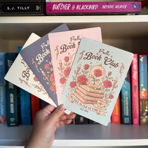 May include: Four Belle's Book Club themed notebooks in various colors: off-white, purple, pink, and light blue. Each notebook features a floral design with roses and the text "Belle's Book Club". The light blue notebook has the text "Tale as Old as Time".