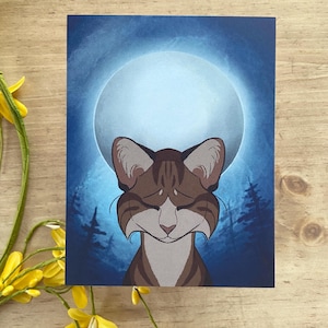 May include: A print featuring a cat with brown and white fur, set against a blue background with a full moon and silhouetted trees. The cat has closed eyes and a serene expression.