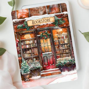 May include: A tablet case with a watercolour illustration of a bookstore in winter. The shop front is decorated with wreaths, snow, and the word "Bookstore" on a sign. The case is surrounded by greenery and a lit candle.