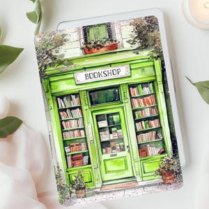 May include: A tablet cover featuring a green watercolour illustration of a bookshop. The shop has a sign that reads "BOOKSHOP" and shelves filled with books. The cover is surrounded by greenery and a lit candle.
