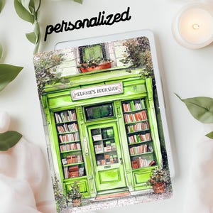 May include: A green and white tablet case featuring a watercolor illustration of a bookstore with the text "Melanie's Bookshop." The word "personalized" is written above the tablet. The case has a bookstore design with books on shelves.