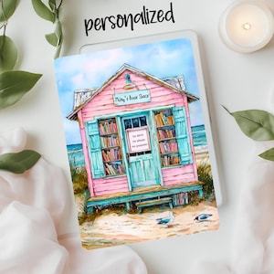 May include: A watercolor painting of a pink beach house with a sign that reads "Miley's Book Shack". The house has a blue door and windows and is surrounded by sand and seagulls.