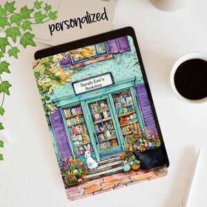 May include: A tablet case featuring a watercolor illustration of a bookstore with the text "Sarah-Lee's Bookshop". The design includes a bunny, flowers, and books. The word "personalized" is written on the top left corner.