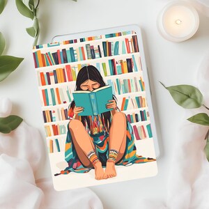May include: A woman sits in front of a bookshelf filled with colorful books, reading a teal blue book. She is wearing a colorful patterned blanket and has long dark hair.