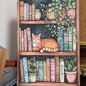 May include: A whimsical illustration of a bookshelf filled with books, potted plants, and a ginger cat napping on a shelf. The background is a dark blue with white stars.