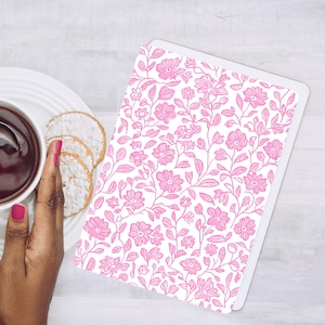 May include: A white tablet with a pink floral pattern. The design features detailed flowers and leaves. A plate with biscuits and a cup of tea are next to the tablet. A hand with pink nail polish is also in the image.