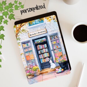 May include: A watercolor illustration of a bookstore with a sign that reads "Michelle's Bookshop". The storefront is decorated with flowers and a white rabbit sits on the steps.