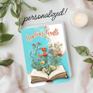 May include: A personalized Kindle cover with a blue background and a white open book with flowers coming out of it. The text on the cover says "Amelia's Kindle".