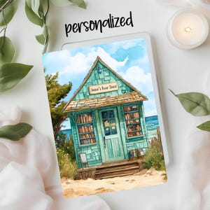 May include: A watercolor illustration of a teal blue beachside book shop with the words "Jassen's Book Shack" above the door. The shop has windows filled with books and a wooden porch with steps leading to the door.