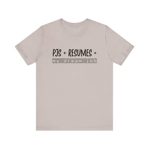 以下が含まれることがあります： 「PJS + RESUMES = my dream job」の黒い文字がプリントされた、薄いベージュ色のTシャツ。半袖でクルーネックです。