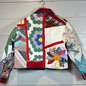 May include: A patchwork jacket constructed from various quilted fabric scraps featuring a mix of floral, plaid, and striped patterns in red, green, blue, yellow, and white. The garment includes a collar, long sleeves, and a button-up front.