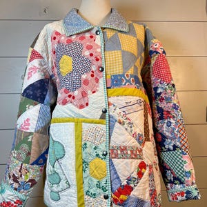 May include: A long-sleeve jacket constructed from various quilted fabric patches in multiple colors and patterns, including floral, gingham, and polka dot prints. The jacket features a light blue collar, a front button closure, and a white base.