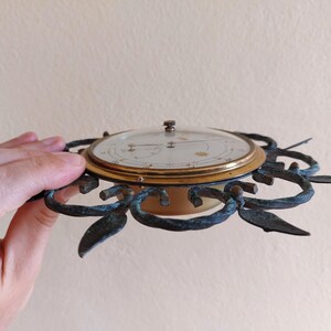 May include: An antique brass and glass clock with a decorative, sunburst-style frame. The clock face is cream-colored with gold accents and a glass cover. The frame has a dark, aged patina.