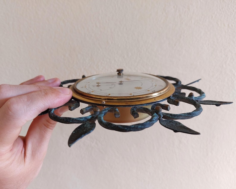 May include: An antique brass and glass clock with a decorative, sunburst-style frame. The clock face is cream-colored with gold accents and a glass cover. The frame has a dark, aged patina.