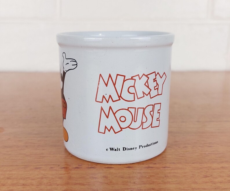 May include: A white ceramic mug with a black handle and the text "But First, Coffee" in a bold, black font. The mug is set against a blurred background, suggesting a cozy setting.