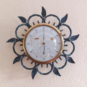 May include: A vintage barometer with a brass-colored frame and a white face, surrounded by a decorative, dark blue metal sunburst design. The barometer displays weather symbols and measurements, adding a touch of classic charm to any space.