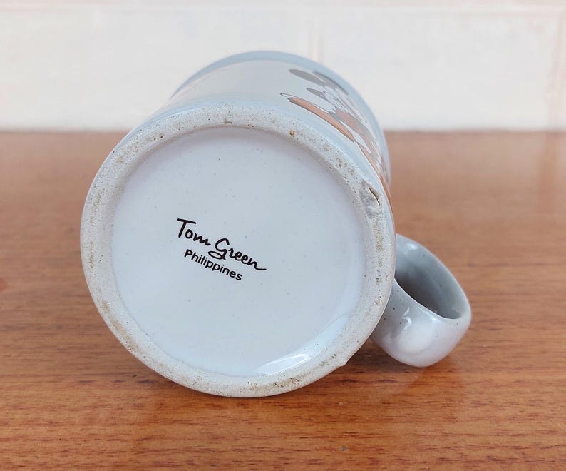 May include: A set of three ceramic mugs with a speckled, matte finish. The mugs are in shades of cream, light gray, and dark gray. Each mug has a simple, minimalist design and a rounded handle.
