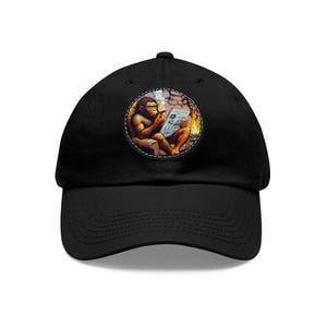 Puede incluir: Gorra de béisbol negra con un parche circular que presenta un dibujo animado de un cavernícola leyendo un periódico junto a una fogata.