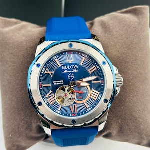 May include: A Bulova Marine Star automatic watch with a blue dial and a blue rubber strap. The watch features Roman numeral hour markers, a visible movement, and the text "AUTOMATIC 21 JEWELS". The watch is water resistant to 200m.