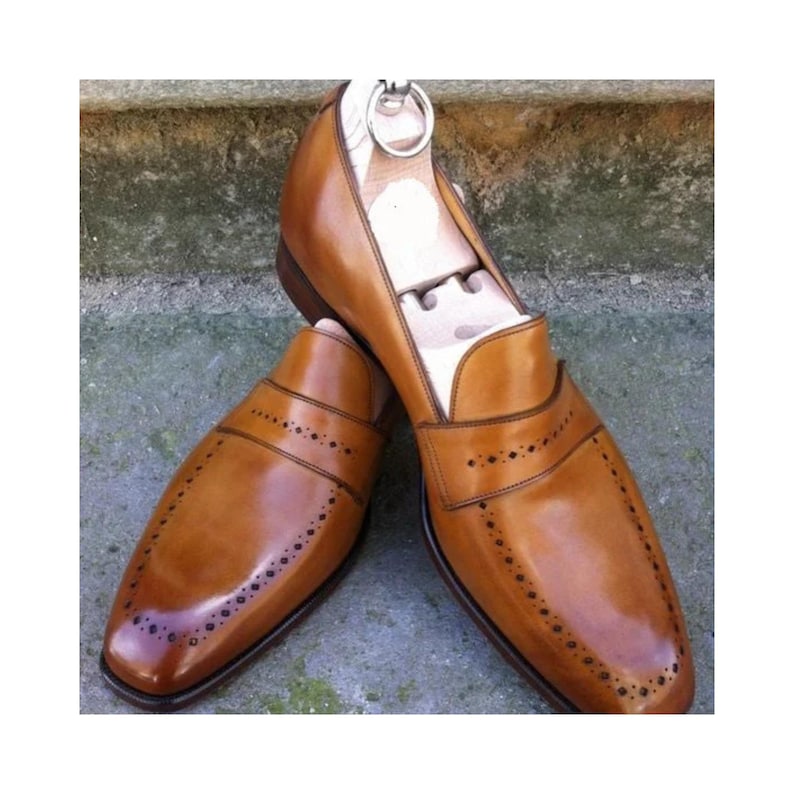 May include: A pair of brown leather slip-on shoes with decorative perforations and a wooden shoe tree inside. The shoes have a polished finish and a classic design, suitable for formal or business attire.
