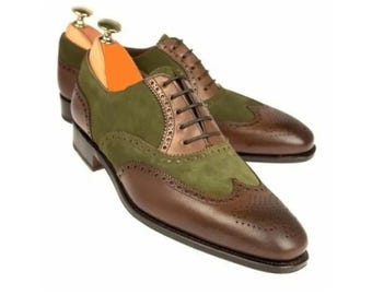 May include: A pair of two-tone leather dress shoes. The shoes feature a brown leather toe and heel, olive green suede midsection, and brown leather accents. The shoes have a classic wingtip design with decorative perforations and brown laces.