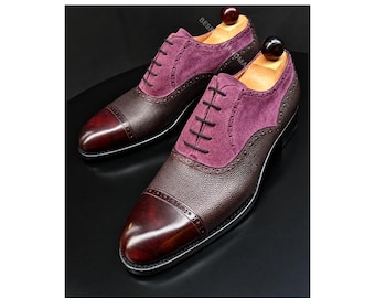 May include: A pair of oxford shoes featuring a deep burgundy leather cap toe, a dark brown textured leather vamp, and purple suede side panels. The shoes have black laces, brogue detailing along the cap toe, and wooden shoe trees inside.